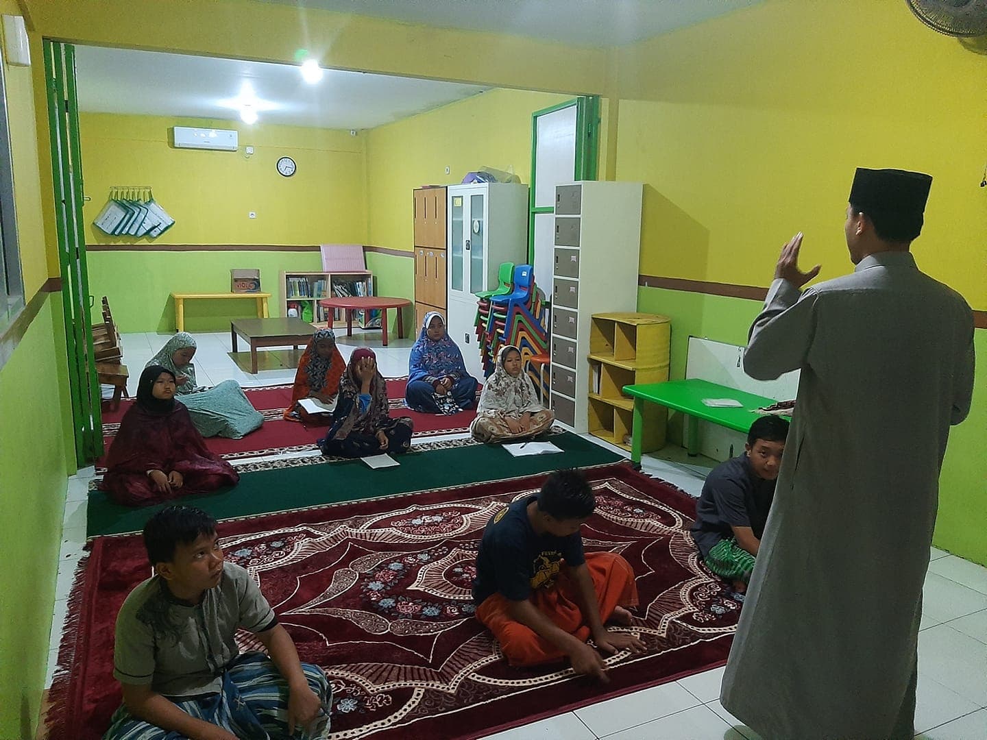 Kelas bahasa Inggris lesehan untuk santri di ruang belajar berkarpet dengan dinding hijau