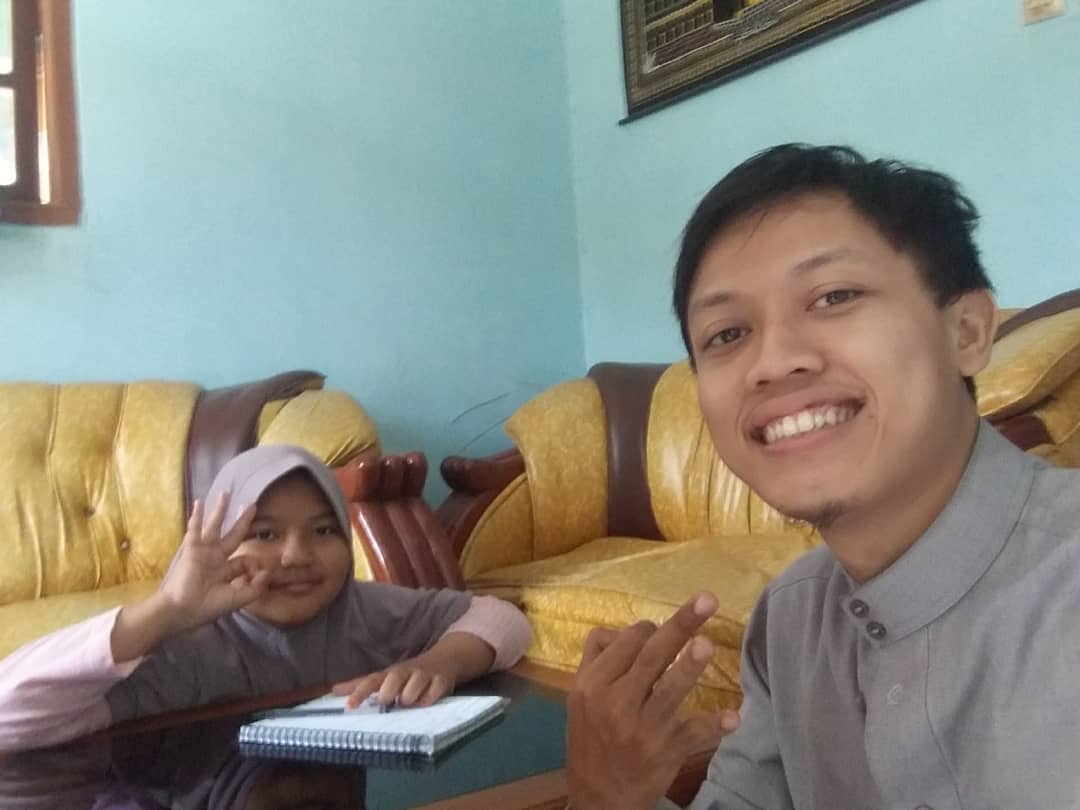 Mr. Dream menemani siswi berkerudung belajar bahasa Inggris dengan buku catatan di sofa kuning
